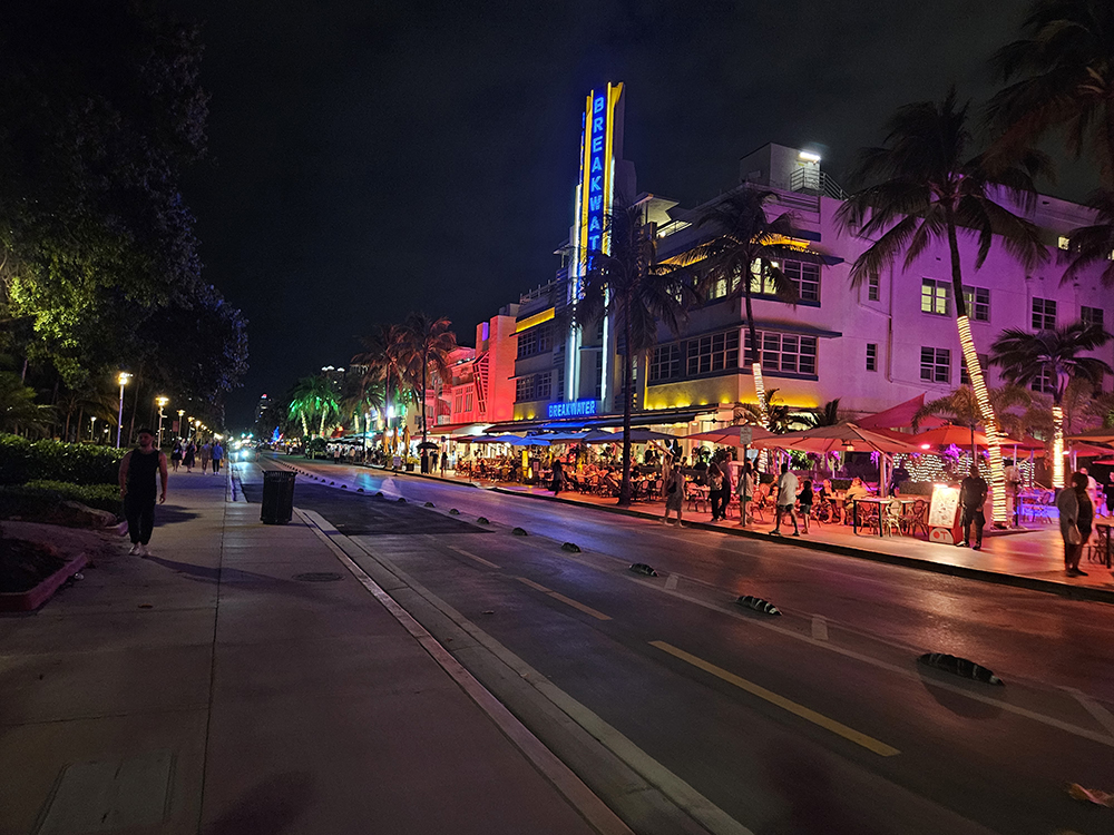 A nighttime photo taken looking south down Ocean Drive. Buildings along the street are lit up in myriad colors.